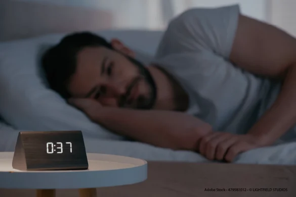 Mann liegt nachts wach im Bett neben Wecker – typische Schlafstörungen bei Schichtarbeit durch gestörten Biorhythmus.